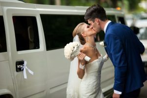 Brunette groom kisses a tiny bride standing before a Rich limousine